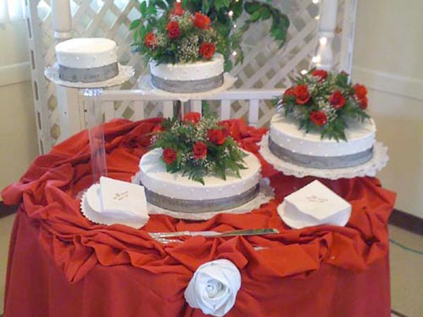 Decorated wedding cake table with red tablecloth, white cakes, and red flower toppers
