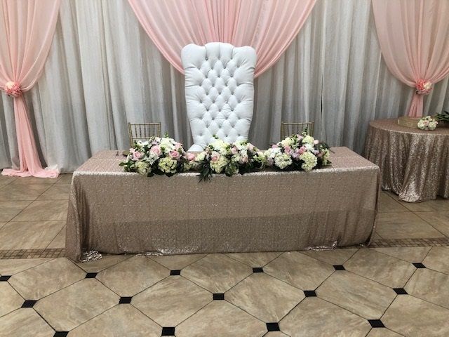 White tufted chair behind a flower-decorated table with pink and gray drapes at a formal event