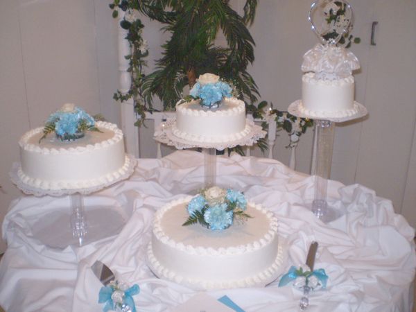 Three white cakes with blue flowers on clear stands at a decorated dessert table