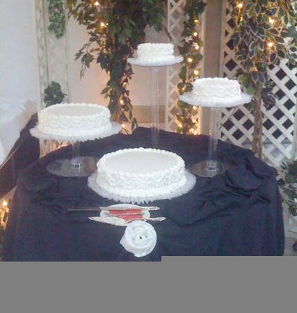 Three white frosted cakes displayed on a black tablecloth at a decorated event table
