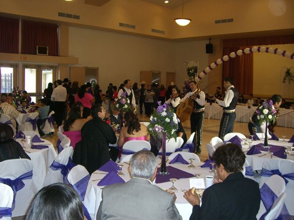 Formal banquet in a hall, with guests seated at white-clothed tables and people mingling near a stage.