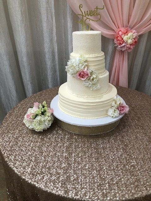 Three-tier white wedding cake with pink flowers on a glittering table, beside a small floral bouquet