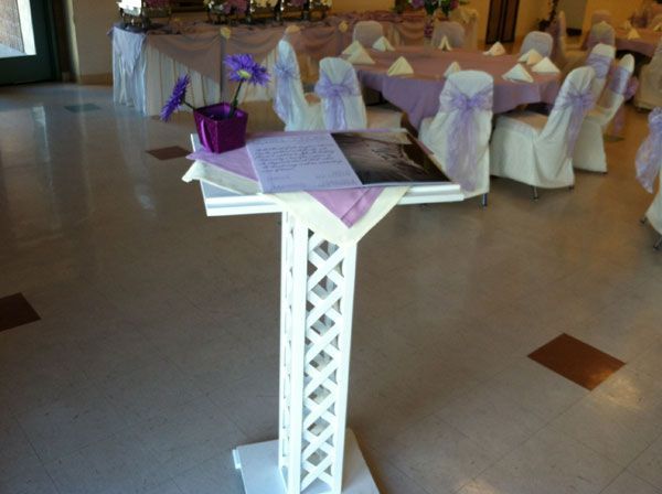 Wedding ceremony podium in a decorated banquet hall with white chair covers and purple accents