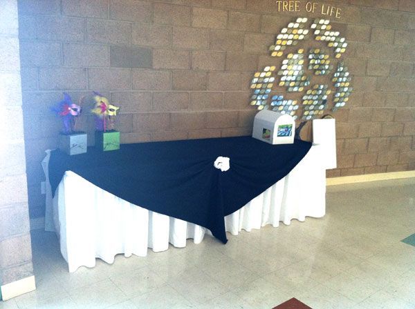 Decorated memorial table with flowers, candles, and a white tree display against a brick wall