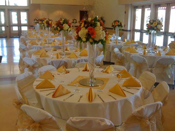 Round banquet tables set with white chairs and gold napkins in a bright event hall