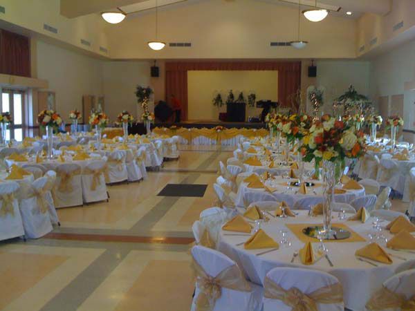 Banquet hall set with round tables, white chair covers, yellow napkins, and floral centerpieces