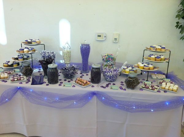 Decorated dessert table with purple accents, cakes, cupcakes, and treats on a white tablecloth