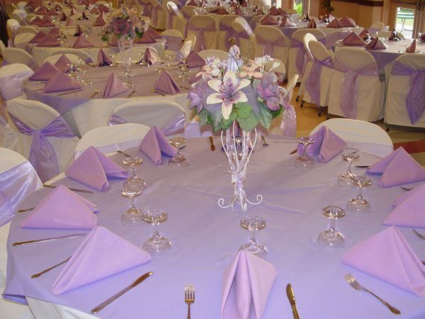 Lavender-decorated banquet tables with folded napkins and a floral centerpiece in a formal dining hall