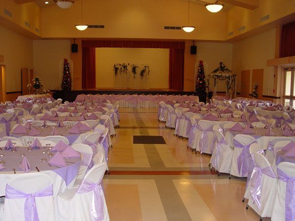 Banquet hall with rows of round tables draped in white and purple, facing a stage with a cross backdrop