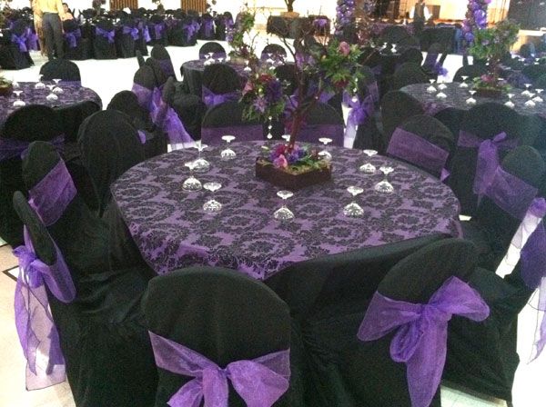 Round banquet tables with purple tablecloths and black chairs tied with purple bows in a decorated event hall