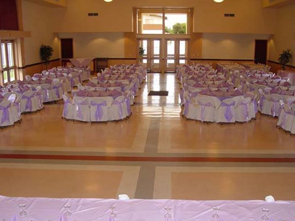 Banquet hall with round tables dressed in lavender linens and chairs, viewed from the front of the room