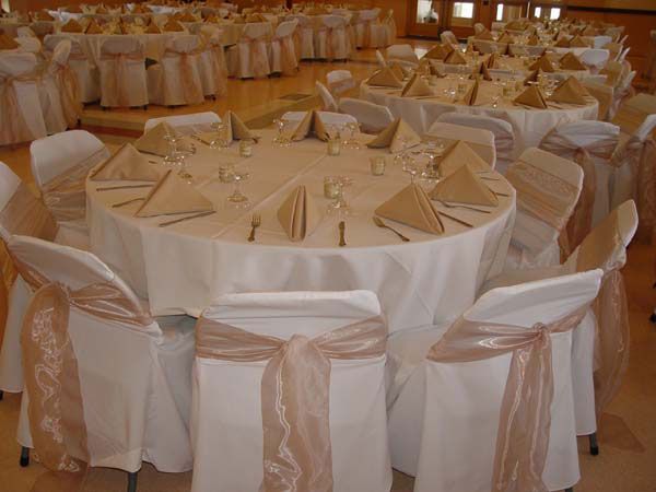 Round banquet tables with white tablecloths and beige chair sashes in a decorated reception hall