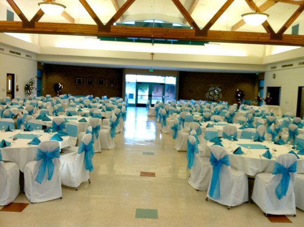 Banquet hall with round tables dressed in white and blue chair bows, set for an event