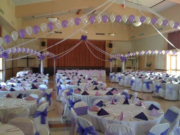 Decorated banquet hall with white tables, purple accents, and balloons set for an event