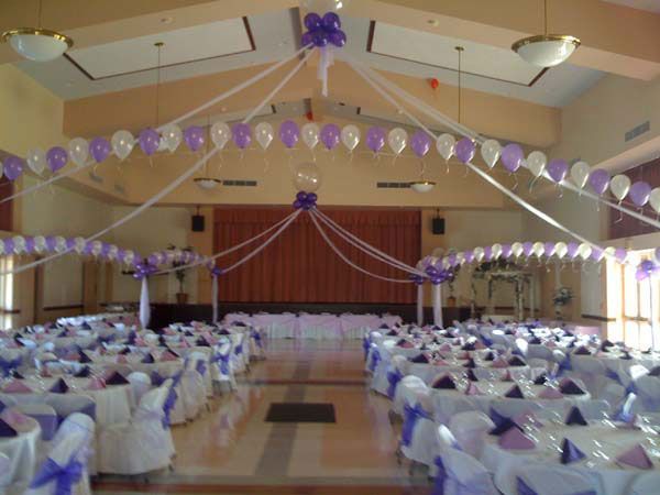 Decorated banquet hall with purple and white balloons and rows of tables facing a stage
