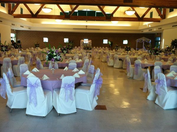 Elegant banquet hall with round tables, white chair covers, and purple floral centerpieces set for an event