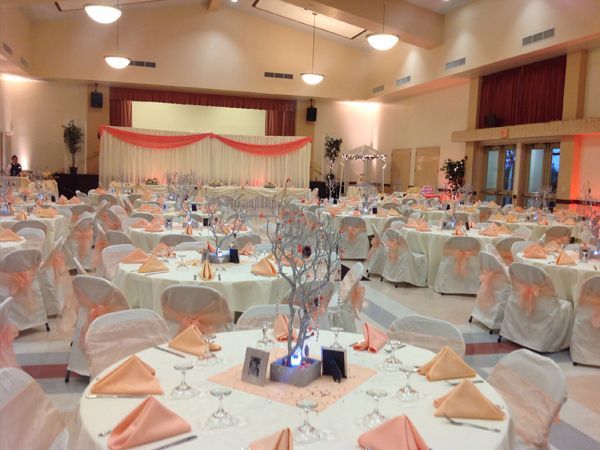 Decorated banquet hall with many round tables, white chair covers, and peach napkins set for an event