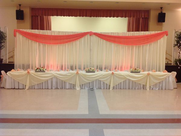 Decorated indoor stage with white drapes and red fabric swags, set for an event