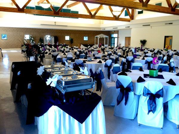 Banquet hall with round tables and white chair covers set for a formal event, guests seated in the background