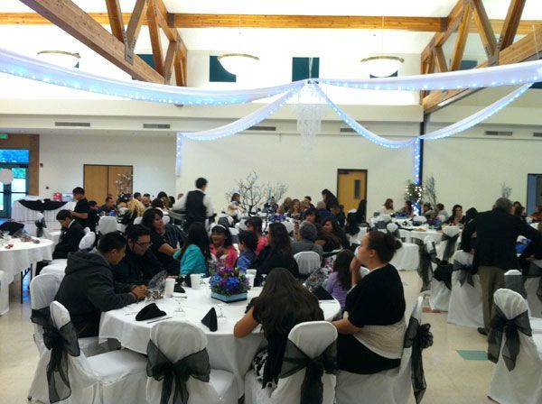 People seated at round tables in a bright banquet hall decorated with white drapes and streamers.