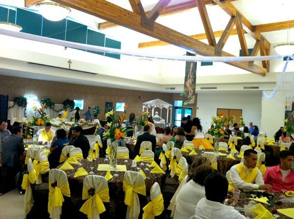 Banquet hall with round tables dressed in yellow and guests seated under wooden beams