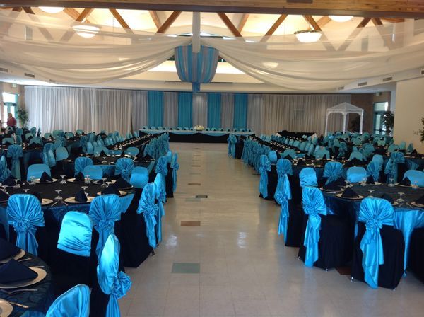 Banquet hall with rows of tables and chairs draped in blue, facing a decorated stage at the front