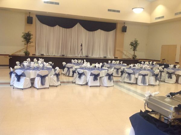 Banquet hall with round tables dressed in white and blue linens in front of a stage with draped curtains