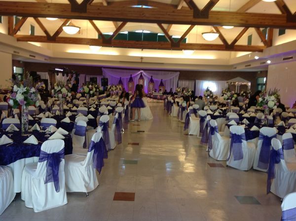 Large banquet hall with rows of white-and-purple chair covers facing a decorated stage for an event
