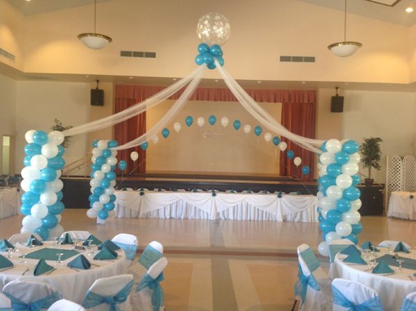 Decorated banquet hall stage with white and blue balloons, draped fabric, and table settings for an event
