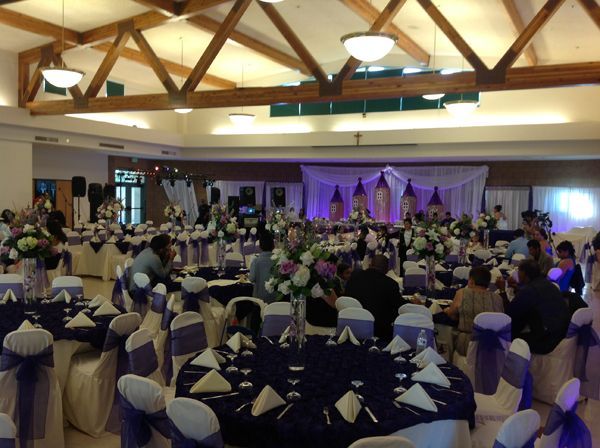 Banquet hall with round tables, purple chair covers, and a decorated stage at the front