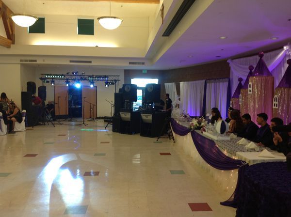 Decorated banquet hall with purple drapes, long tables, and a lit stage at the far end