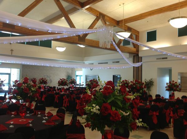 Decorated banquet hall with red floral centerpieces and draped white ceiling fabric