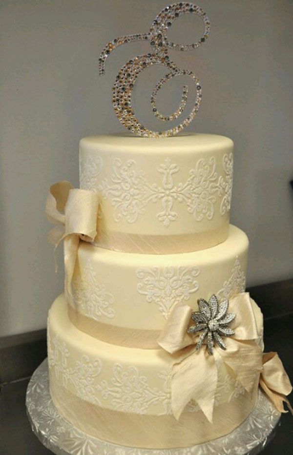 Three-tier ivory wedding cake with white floral decorations and a jeweled number 80 topper