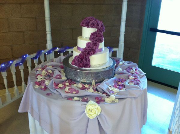 White tiered cake with purple floral decorations on a round table at a celebration