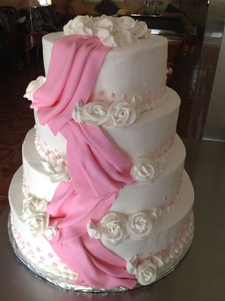 Three-tier white wedding cake with pink draped fondant and white roses