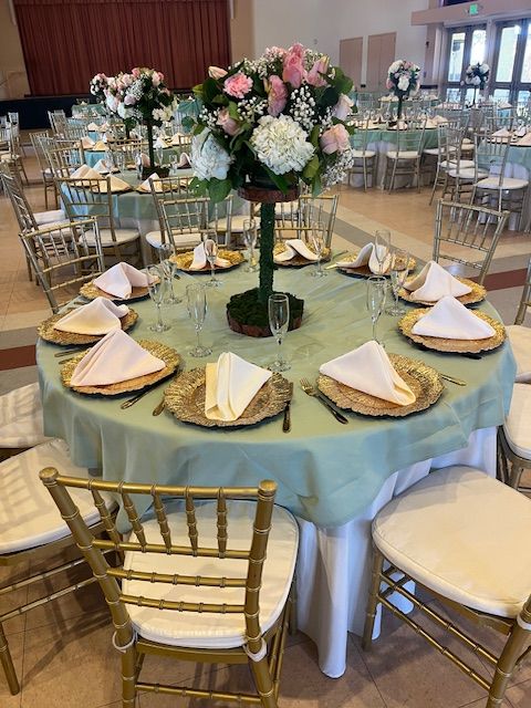 Round banquet table set with gold chairs, pale blue linen, folded napkins, and a floral centerpiece