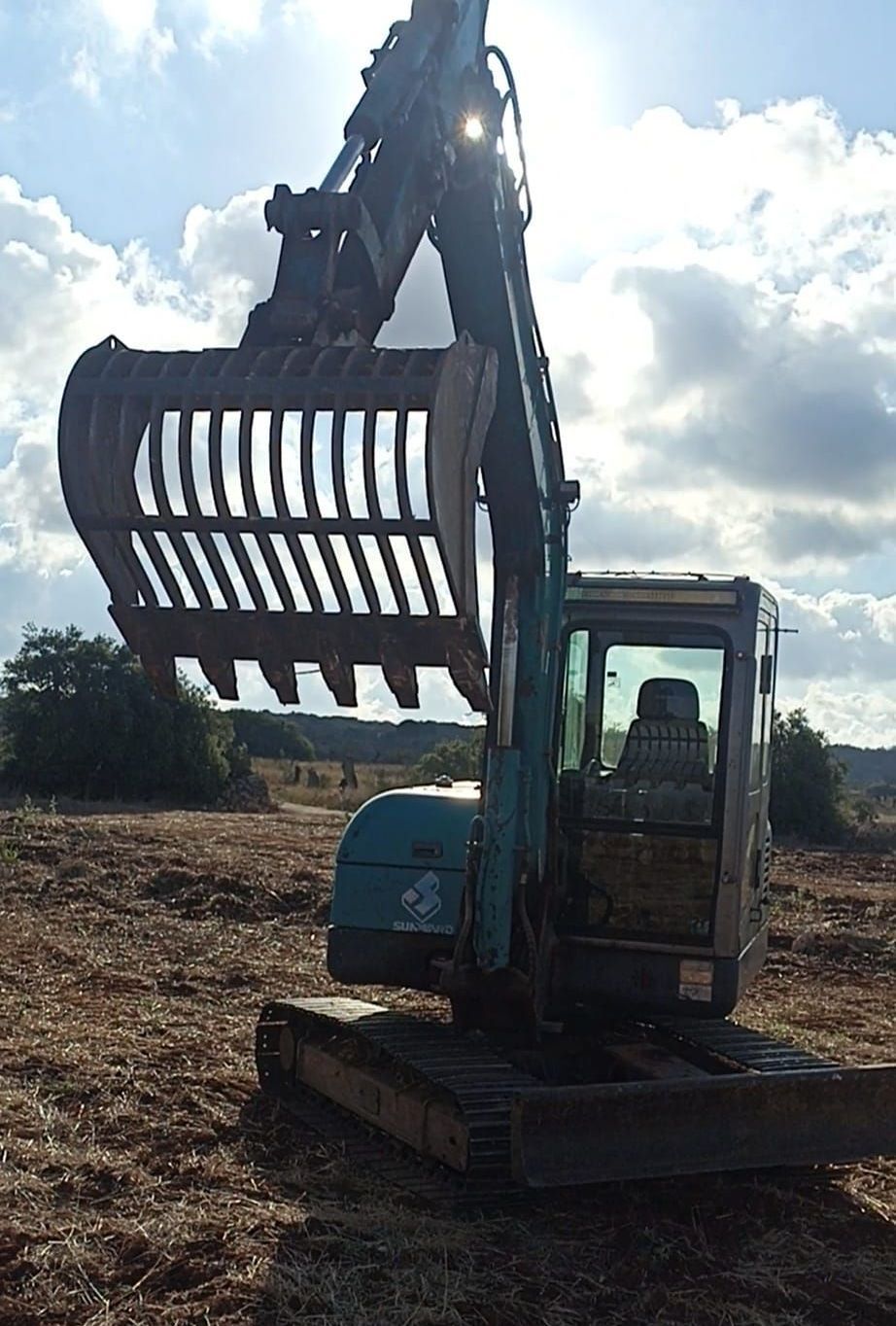 Un escavatore con una grande benna è seduto in un campo.