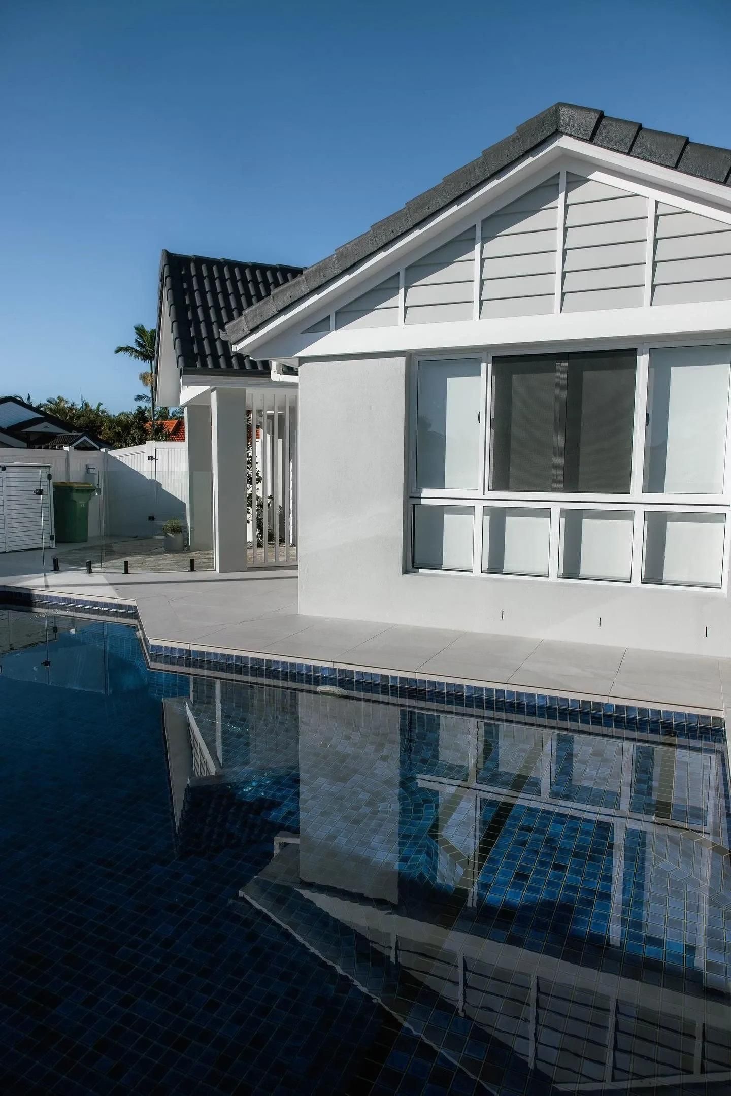 A modern house with a pool, reflecting the building in the water. Blue sky.