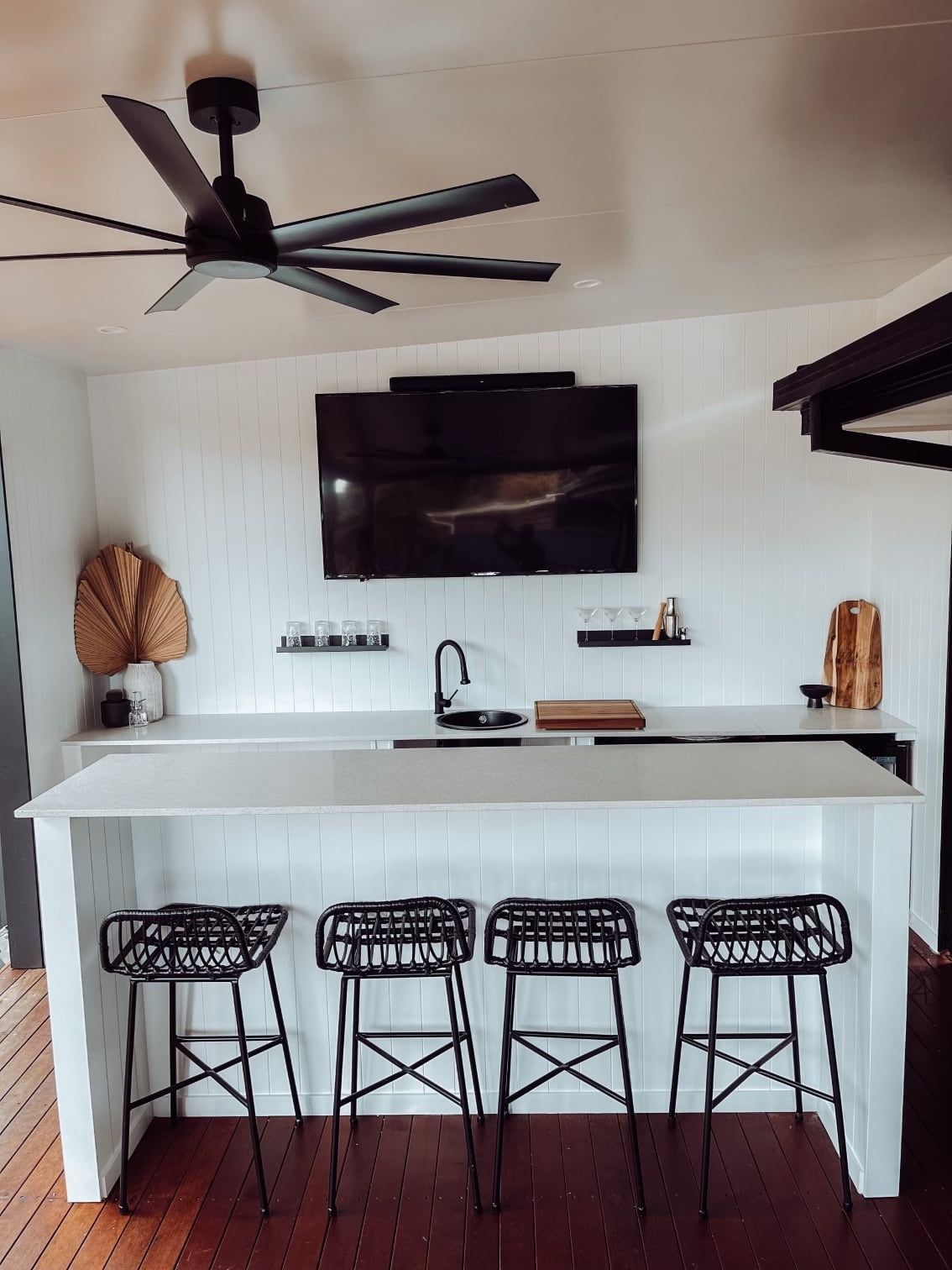 an outdoor kitchen with a ceiling fan and a flat screen tv