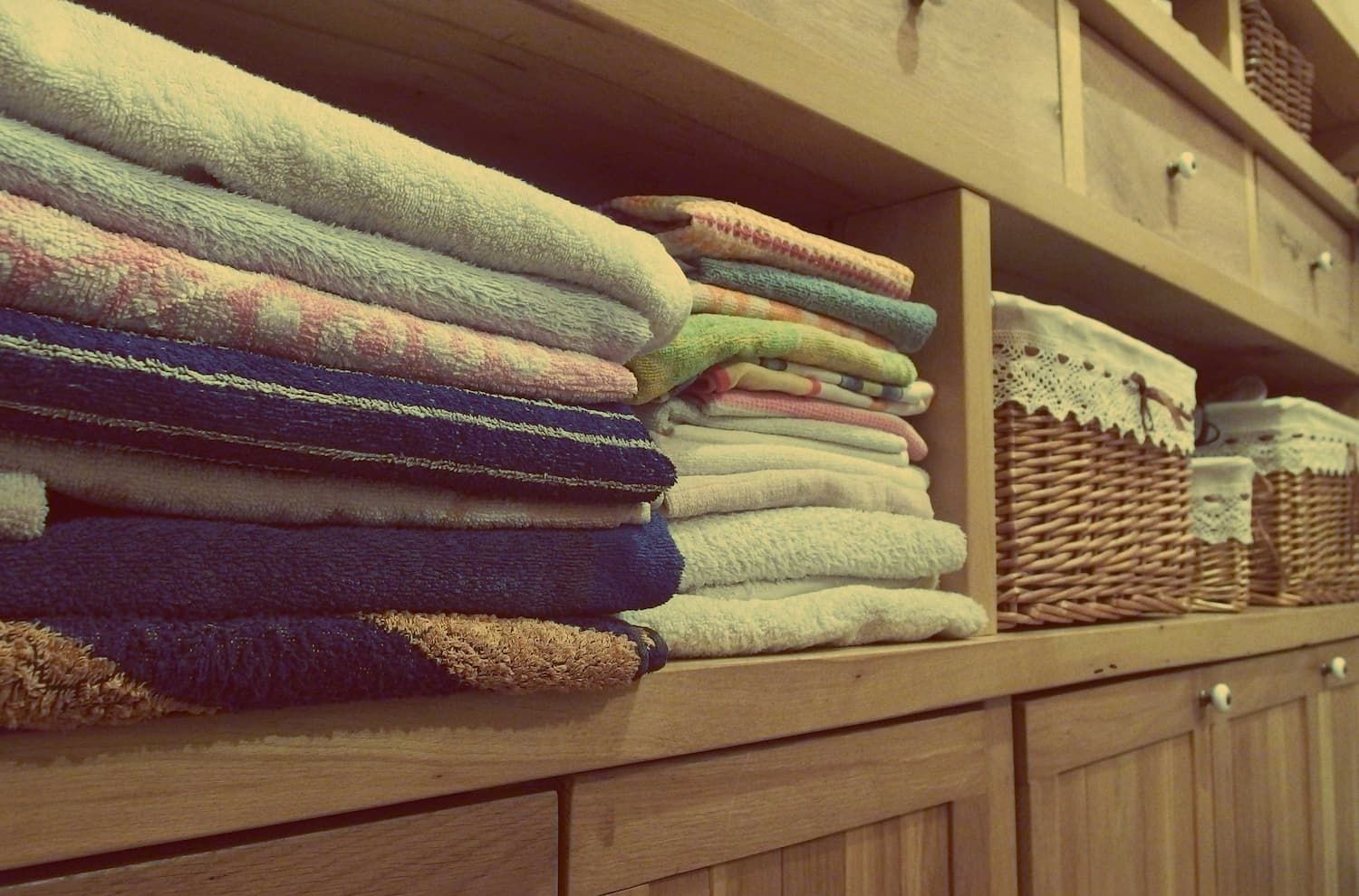 a stack of towels sits on a wooden shelf next to wicker baskets