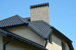 A brick house with a black roof and a chimney on the roof.