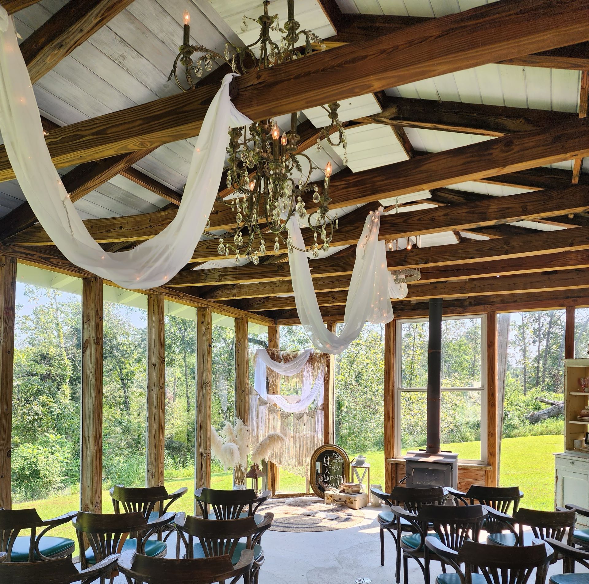 An outdoor wedding venue with wooden beams, draping fabric, chandelier, and chairs facing an altar.