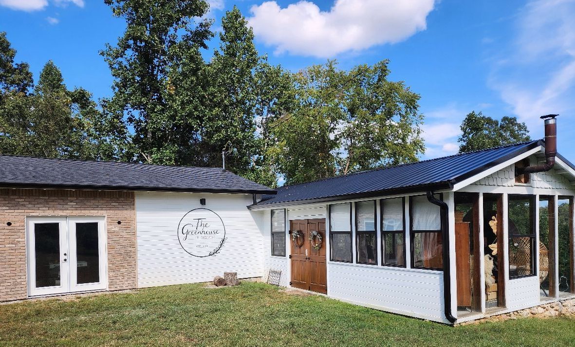White building with brick and screened porch, trees, blue sky.