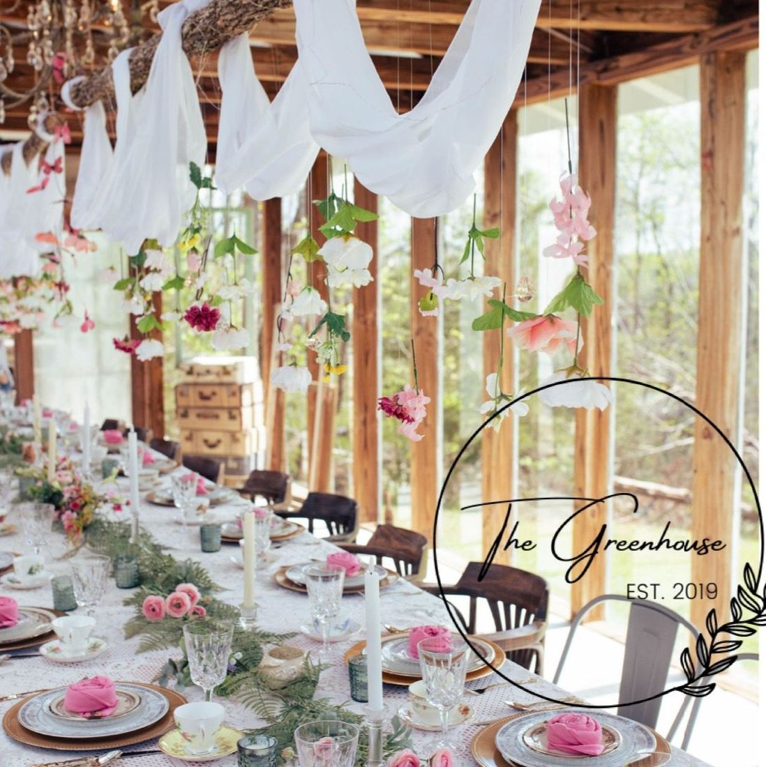 Elegant greenhouse dining scene with hanging flowers, long table, and floral decor.