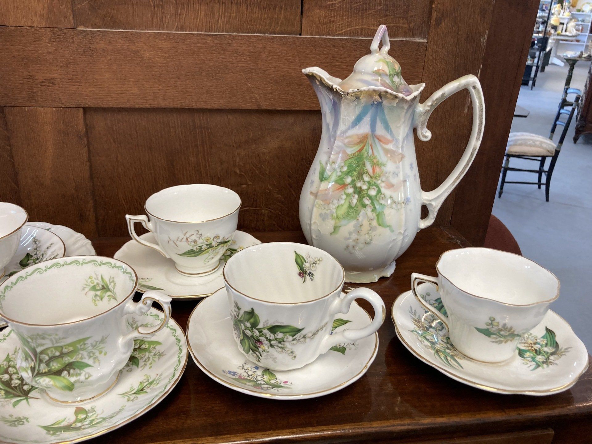 Tea set with cups, saucers, and a pitcher decorated with lily of the valley on a wooden surface.