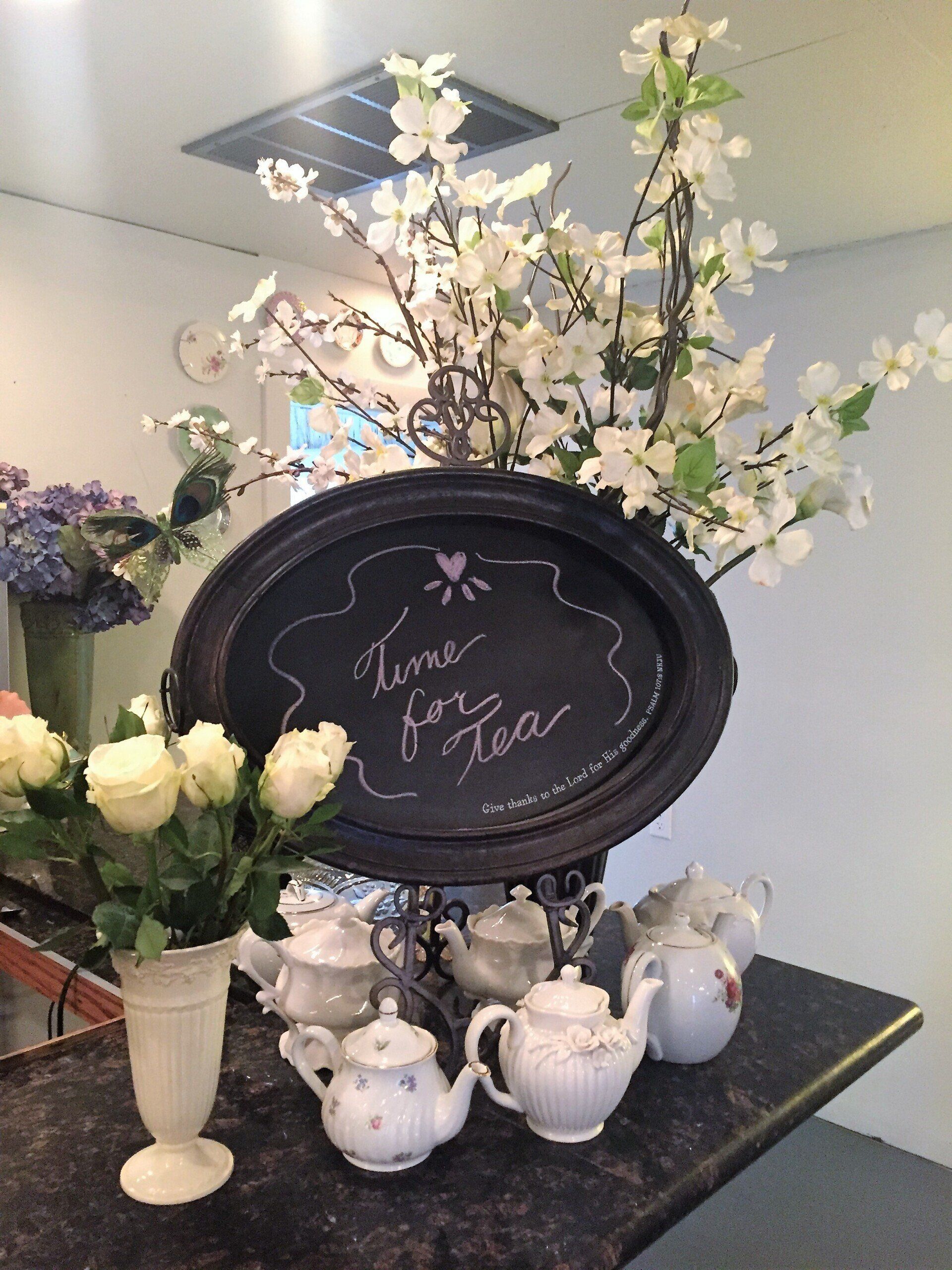 Teapots and flowers arranged on a counter, with a chalkboard sign that says 