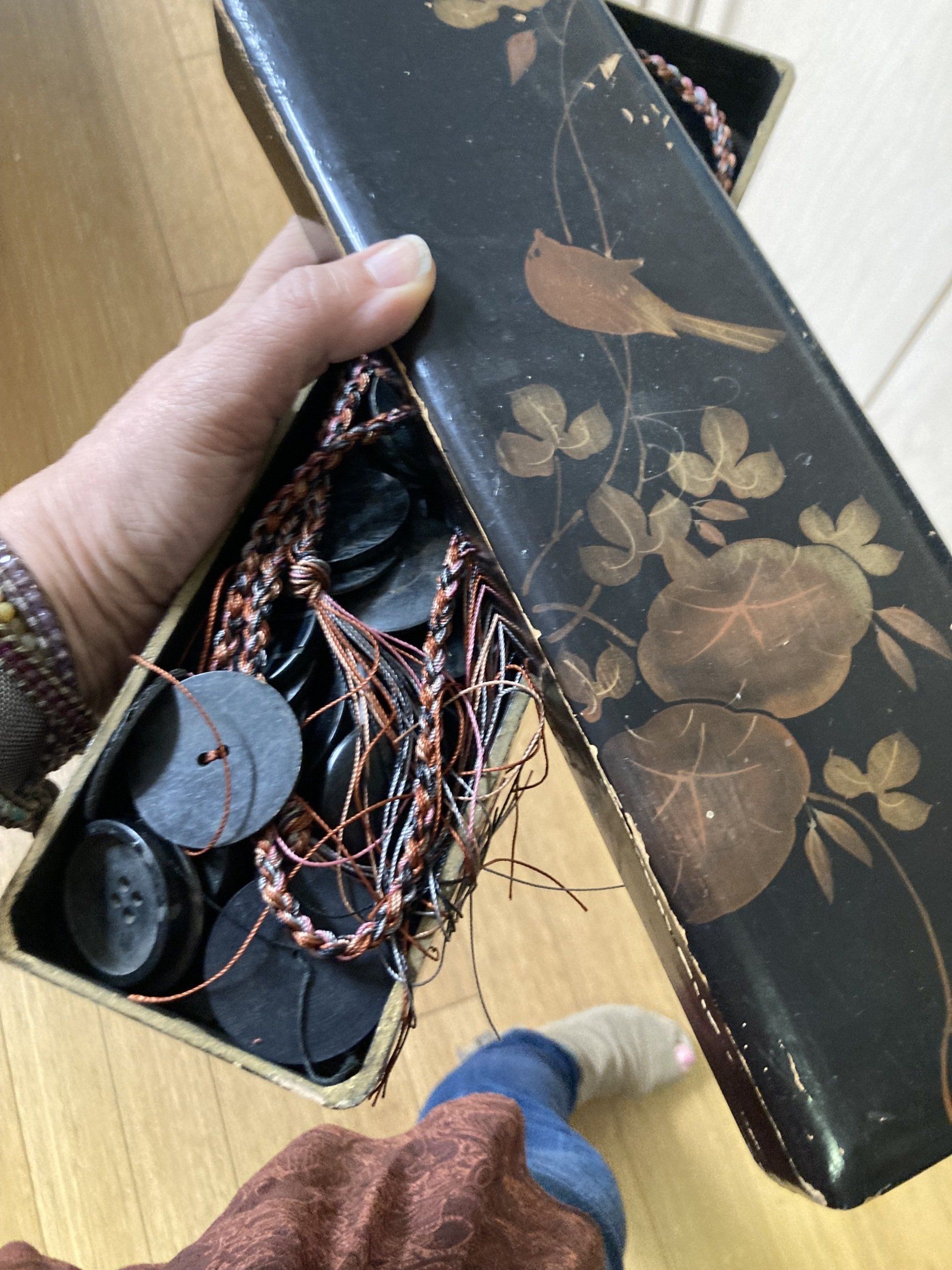 Person holding a black decorative box with a bird and floral design, filled with black disks and string.