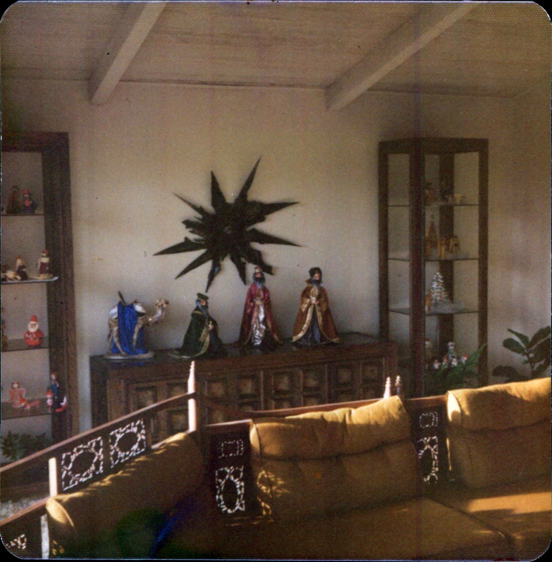 Living room with a wood cabinet displaying three kings, a starburst, and a glass cabinet. Brown sofa in the foreground.