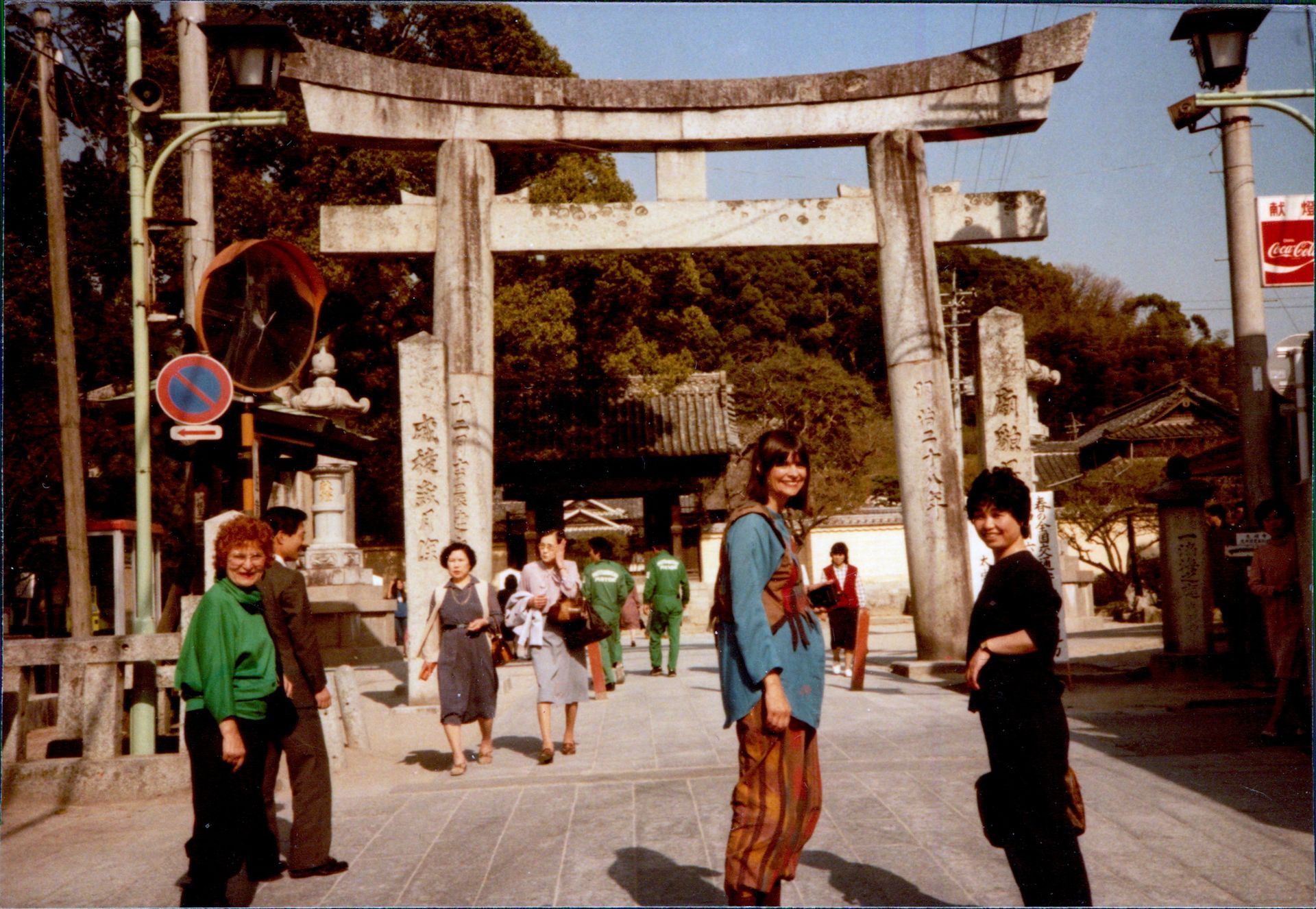 People standing near a stone torii gate in Japan, with other people walking in the background.