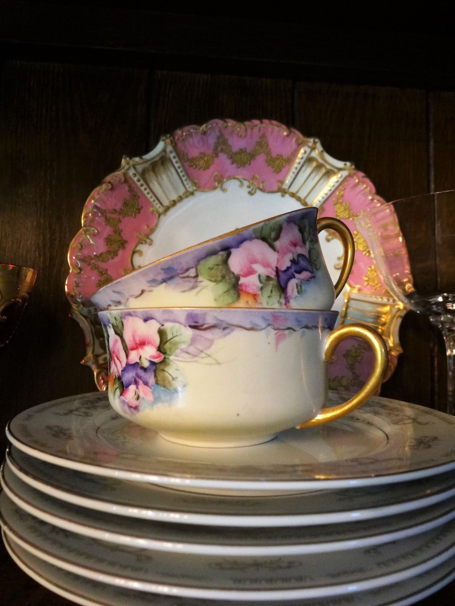 Antique china The china features delicate hand-painted floral motifs, specifically purple, pink, and yellow pansies with green foliage, accented by gold trim on the handles and edges. 
